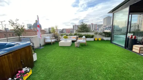 Terraza con césped artificial verde, jacuzzi, muebles de exterior y vistas urbanas. Ideal para aprender como limpiar césped artificial terraza.
