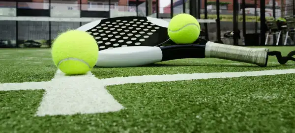 Raqueta de pádel y pelotas sobre césped artificial padel. La cancha está lista para el juego.